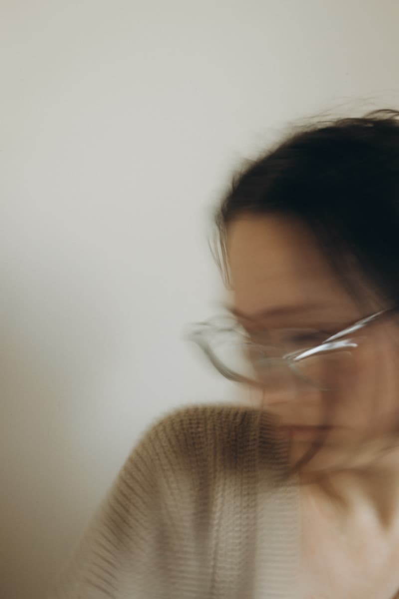 Self-portrait in glasses and a knit cardigan, face dissolving in motion